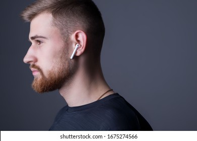 Closeup portrait of a young bearded guy of twenty-five years old, standing in profile. In wireless white headphones. Sporty style. Athletes headphone promotional photo