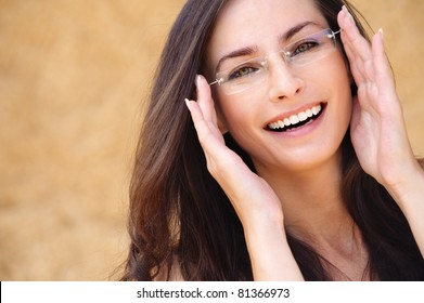 Close-up portrait of young beautiful brunette woman wearing glasses against beige background.