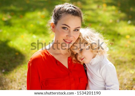 Closeup portrait of a young beautiful brunette woman with little curly daughter in autumn park
