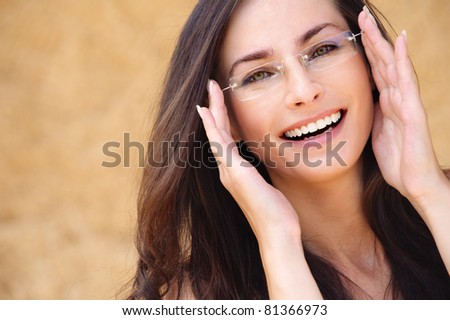Close-up portrait of young beautiful brunette woman wearing glasses against beige background.