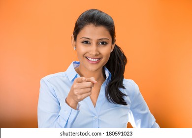 Closeup portrait of young, beautiful, excited, happy woman smiling, laughing, pointing finger towards you, camera gesture, isolated on orange red background. Positive human emotion, attitude, reaction
