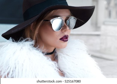 Closeup portrait of young beautiful fashionable woman with sunglasses. Lady posing on dark grey background. Model wearing stylish wide-brimmed hat, jacket. Girl looking at camera. Female fashion.Toned