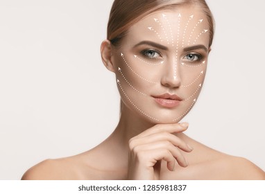 التجميل بالفيلر عن طريق الحقن لإستعادة شباب البشرة 4 صورة عن قرب لامرأة شابة وجميلة وصحية مع الأسهم على وجهها. مفهوم السبا والجراحة وشد الوجه والعناية بالبشرة
