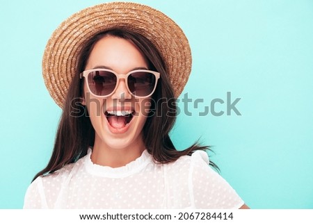 Closeup portrait of young beautiful smiling female in trendy summer dress.Sexy carefree woman posing near blue wall in studio.Positive model having fun indoors.Cheerful and happy in sunglasses and hat