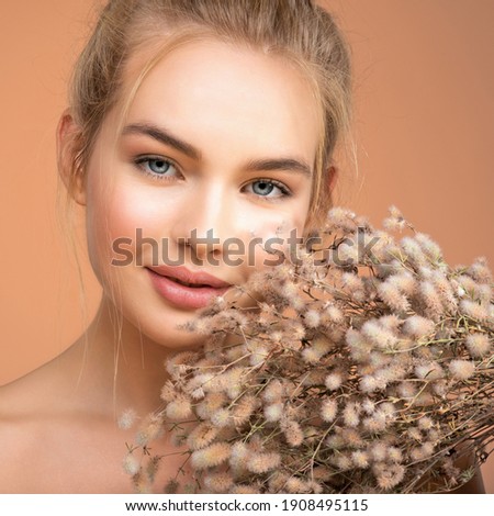 Closeup portrait of young beautiful woman with a healthy  skin of the face. Blonde girl with a bunch spring dry field flowers near the face - over colored background. Beauty face care concept.