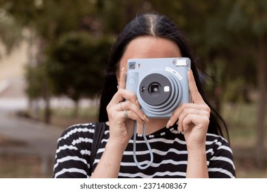 Close-up portrait of a young brunette girl on the street. She is holding a vintage Polaroid camera. A student takes pictures with a camera. - Powered by Shutterstock