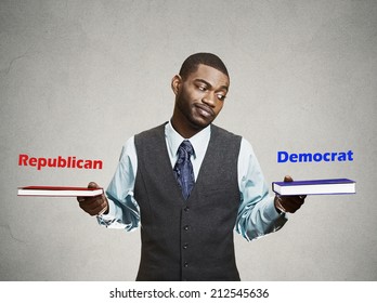 Closeup Portrait Young Business Man, Confused Student Holding Red And Blue Book In Each Hand, Thinking Hard, Deciding Which One To Choose, Way To Go, Isolated Grey Wall Background. Face Expression