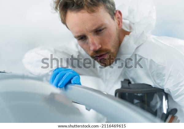 Close-up portrait of a young car painter\
checking the quality of automobile bumper\
paintwork