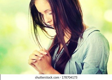 Closeup portrait of a young caucasian woman praying, against abstract green background