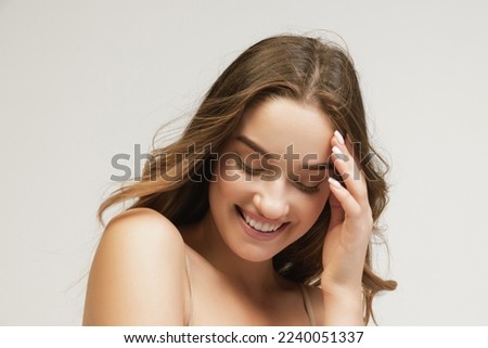 Closeup portrait of young cheerful beautiful girl with curly long hair smiling and looking at camera with happy and relaxed face expression. Health, beauty, fashion and ad concept