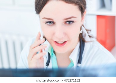 Closeup portrait of a young female doctor consulting with colleague on the mobile telephone looking at x ray.