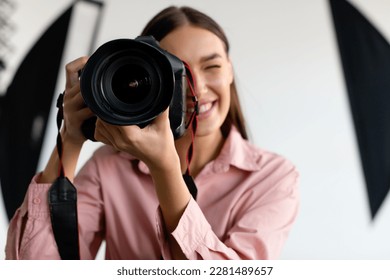 Closeup portrait of young female photographer taking photo, lady working at photostudio with lighting equipment, using professional dslr camera, white background, copy space - Powered by Shutterstock