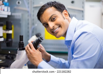 Closeup portrait, young friendly scientist looking into microscope. Isolated lab background. Research and development sector