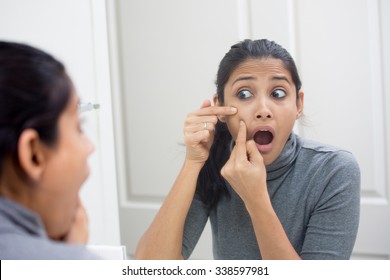 Closeup portrait of young frustrated woman surprised stunned to see zit on her face, gray turtleneck, isolated mirror reflection background. Facial  feelings, situation, reaction