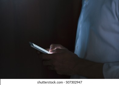 Close-up Portrait Of Young Handsome Man Using Smart Phone In Hand On Dark Background