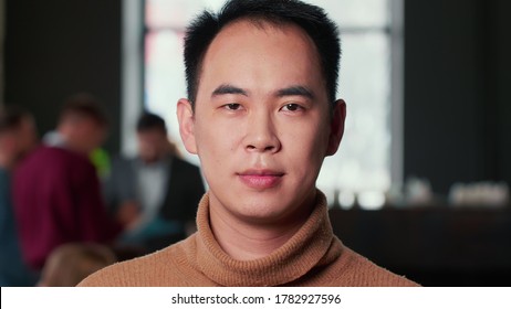 Close-up portrait of young happy Asian entrepreneur businessman looking at camera smiling at modern trendy loft office.
