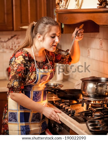 Closeup portrait of young housewife tasting soup from pan on fire