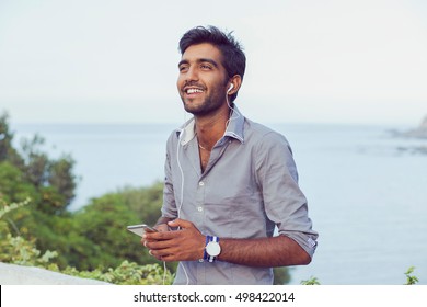 Closeup Portrait Young Indian Asian Male College Student Indian Teenage Boy Listening To Music Audio Books Studying On His Phone Player With Headphones, Outdoors Background