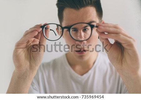 Closeup portrait of young man with glasses.  Handsome guy is holding his eyeglasses right in front of camera with one hand. The concept is isolated on a white background.