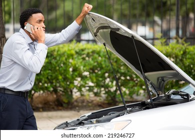 Closeup portrait, young man having trouble with his broken car, opening hood and calling for help on cell phone, isolated green trees outside background