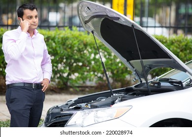 Closeup Portrait, Young Man Having Trouble With His Broken Car, Opening Hood And Calling For Help On Cell Phone, Isolated Green Trees Outside Background