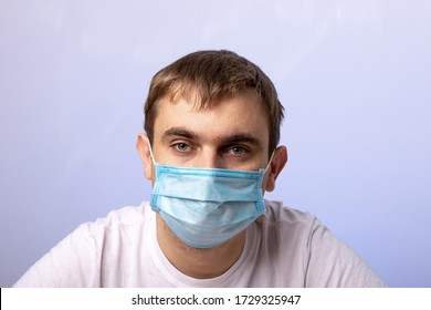 Close-up Portrait Of A Young Man In A Medical Mask. A Painful Look. Blue Background. Quarantine. Emotions: Fatigue, Lethargy, Apathy