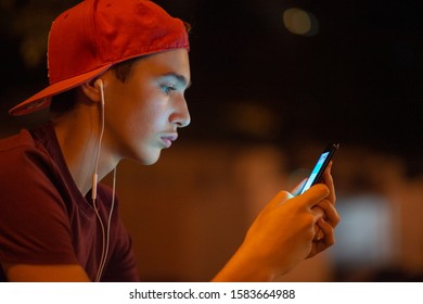 Close-up Portrait Of A Young Man With Smartphone, In The City.   Teenage Boy Is Using Phone, Outdoors At Night.  Caucasian Teenager In Casual Clothes With Cell Phone, Urban Scene. Soft Focus