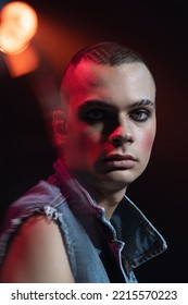 Close-up Portrait Of Young Man Wearing Makeup, Smokey Eyes, Posing Isolated Over Dark Background In Neon. Spot Light. Concept Of Fashion, Freedom Of Choice, Lifestyle, Lgbt, Generation Z, Trends