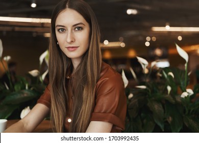 Close-up Portrait Of Young Modern Businesswoman In Stylish Brown Dress, Sitting In Cafe, Drinking Coffee, Enjoying Conversation, Day-off. Restaurant Manager Talking To Employees, Smiling Pleasantly