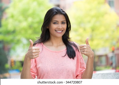 Closeup portrait of young pretty woman in pink shirt with two thumbs up sign gesture, isolated outdoors background. Positive emotion facial expression feelings, signs and symbols, body language