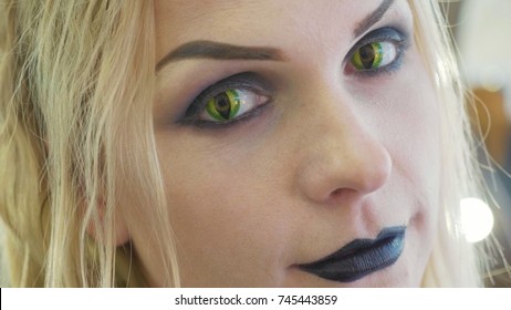 Close-up portrait of young pretty woman with halloween makeup at beauty salon. Face of lady with cat eyes contact lenses.