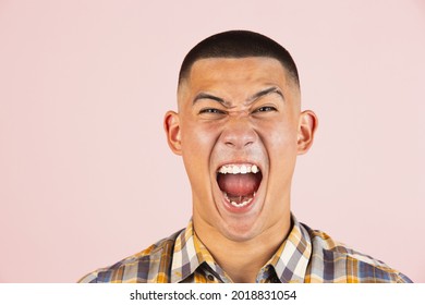 Close-up portrait of young screaming, shouting asian man, guy in a plaid shirt isolated over light pink studio background. Concept of human emotions, leisure, youth.