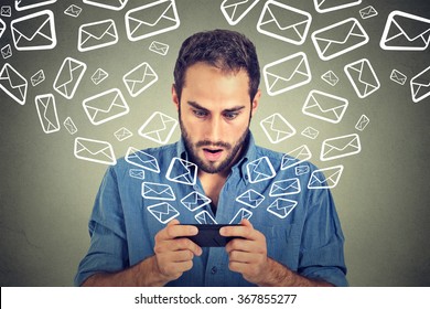 Closeup portrait young shocked man busy sending messages emails from smart phone email icons flying of mobile phone isolated on gray wall background. Telecommunications, internet, data plan concept