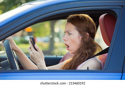 Closeup Portrait, Young Shocked, Stressed Woman Driver, Driving In Car Checking Smart Phone Annoyed By Bad Text Message Email Isolated Outside Street Background. Negative Human Emotion Face Expression