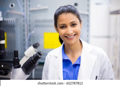 Closeup portrait, young smiling scientist in white lab coat standing by microscope. Isolated lab . Research and development.