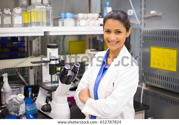 Closeup portrait, young smiling scientist in\
white lab coat standing by microscope. Isolated lab background.\
Research and\
development.