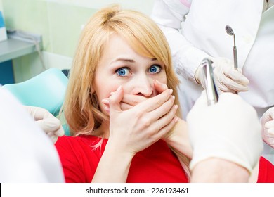 Closeup portrait young terrified girl woman scared at dentist visit, siting in chair, covering her mouth, doesn't want dental procedure, drilling, tooth extraction, isolated clinic office background - Powered by Shutterstock