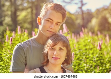 Close-up Portrait Of A Young White Couple In Their Early 20s Against The Backdrop Of An Evening Garden In Sunny Summer Weather.