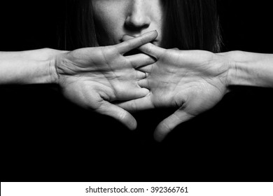 Closeup Portrait Of Young Woman Hiding Mouth By Hands, Showing Speak No Evil Concept, Isolated On Black Background. Human Emotion, Expression, Rights, Communication. Copy-space. Monochrome Studio Shot