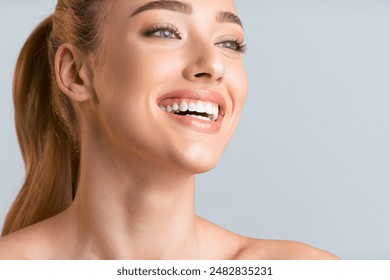 A close-up portrait of a young woman with light brown hair pulled back in a ponytail, smiling brightly. Her skin is fair and glowing, and her teeth are white and bright, copy space - Powered by Shutterstock