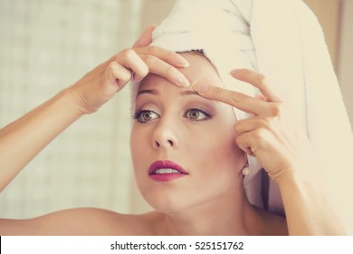 Closeup Portrait Of Young Woman Looking In A Mirror Squeezing An Acne Or Blackhead On Her Face. 