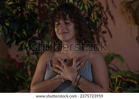 Close-up portrait of a young woman meditating with eyes closed with her hands resting on her chest in a low light setting