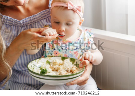 Closeup portrait of young woman mother feeding her girl daughter with vegetables broccoli cauliflower. Healthy organic food for children. Candid lifestyle family life. Baby trying finger food