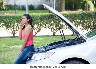 Closeup Portrait, Young Woman In Pink Tanktop Having Trouble With Her Broken Car, Opening Hood And Calling For Help On Cell Phone, Isolated Green Trees And Shrubs Outside Background