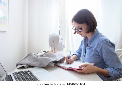 Closeup portrait of young woman seamstress sitting and sews on sewing machine.Dressmaker work on the sewing machine.Tailor making a garment in her workplace. Hobby sewing as a small business concept. 