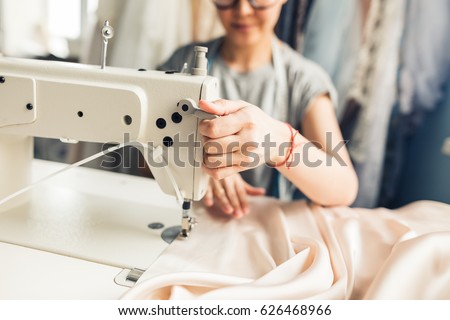 closeup portrait of young woman seamstress sitting and sews on sewing machine. Dressmaker work on the sewing machine. Tailor making a garment in her workplace. Hobby sewing as a small business concept