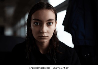 Close-up portrait of a young woman with a serious expression. Dark, moody lighting emphasizes her gaze, creating a contemplative and emotional atmosphere. Perfect for themes of emotion and intensity. - Powered by Shutterstock