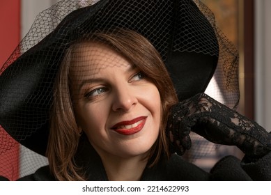 Close-up Portrait Of Young Woman Wearing Black Wide-brimmed Hat With Veil And Lace Gloves With Red Lipstick. Girl From High Society