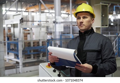 Close-up Portrait of a young worker in a factory. Engineer or Technician man in workwear and hard hat holding paper documents standing in control room