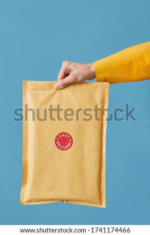 Close-up of postman holding parcel packed in paper isolated on blue background